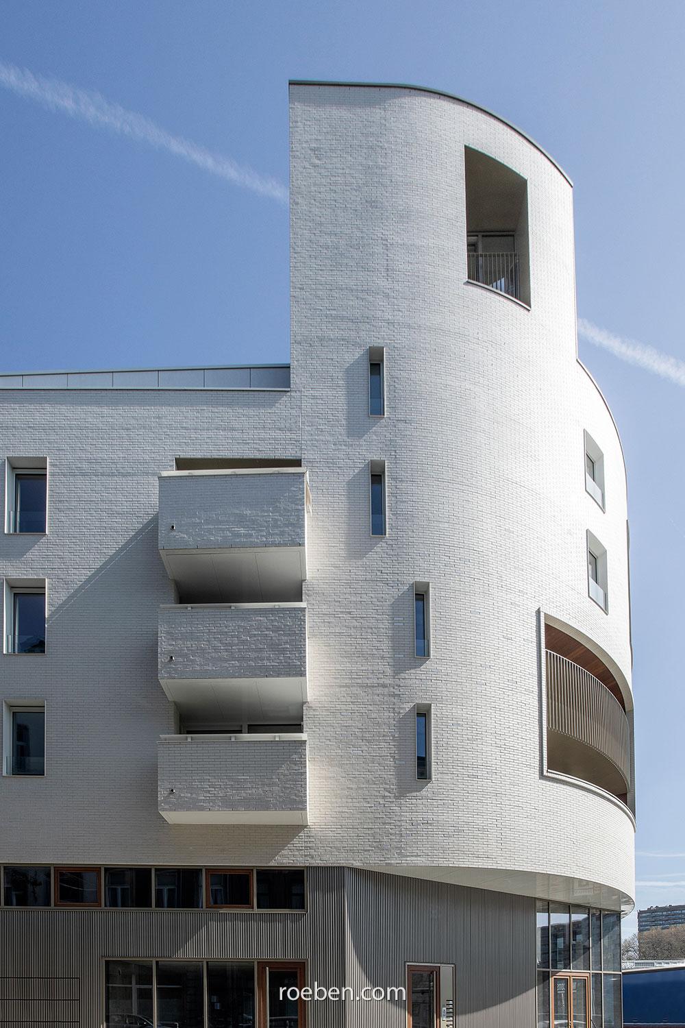 Modernes weißes Gebäude mit geschwungenen Balkonen vor blauem Himmel.