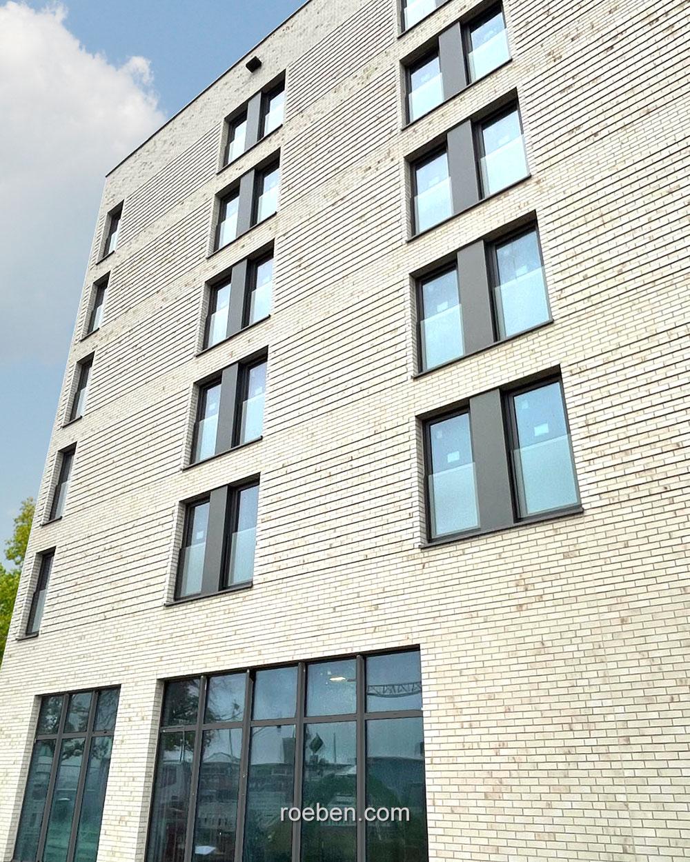 Mehrstöckiges Gebäude mit grauen Ziegelwänden und großen Fenstern.