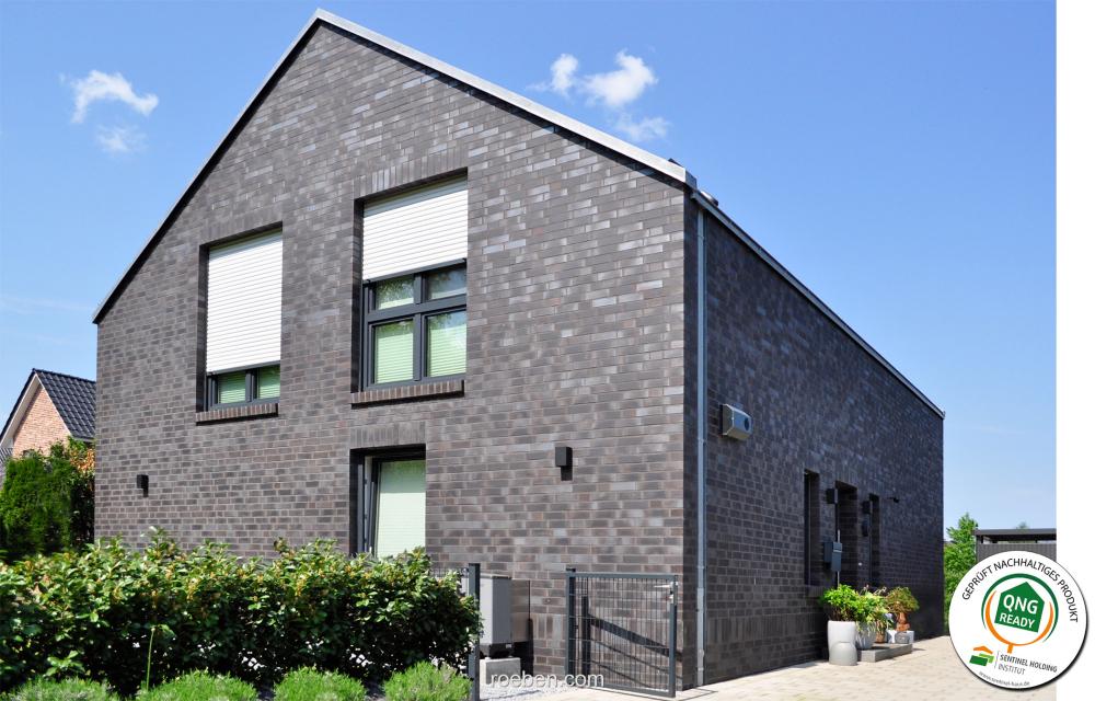Modernes schwarzes Ziegelhaus vor blauem Himmel, umgeben von Grün mit QNG-Siegel