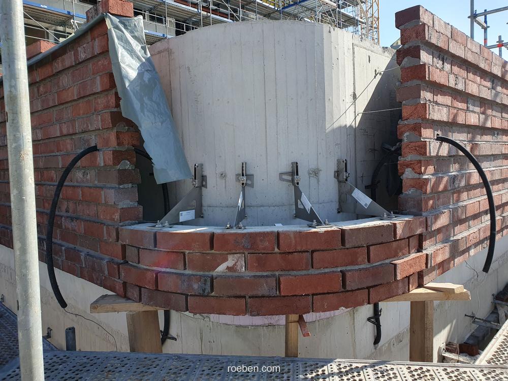 Runde Backsteinmauer im Bau, mit grauer Abdeckung und Metallstangen.