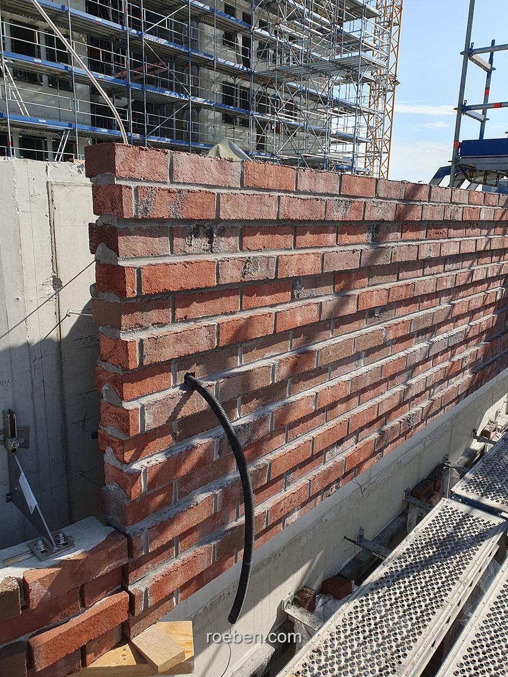 Ziegelmauer im Bau vor einem Gerüst bei Sonnenschein.