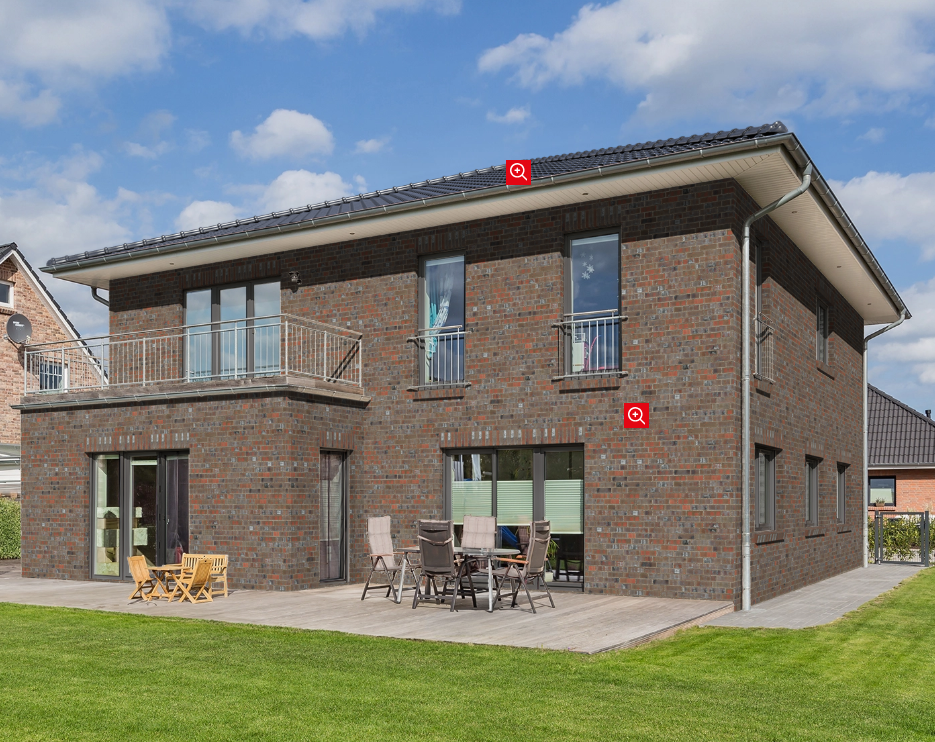 Zweistöckiges Backsteinhaus mit Terrasse und Garten bei blauem Himmel.
