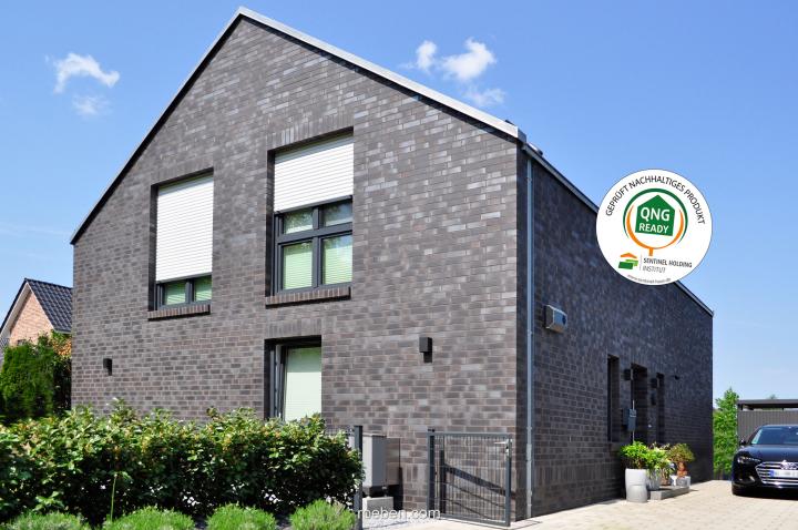 Modernes, graues Backsteinhaus mit Garten und Auto und QNG-ready-Siegel