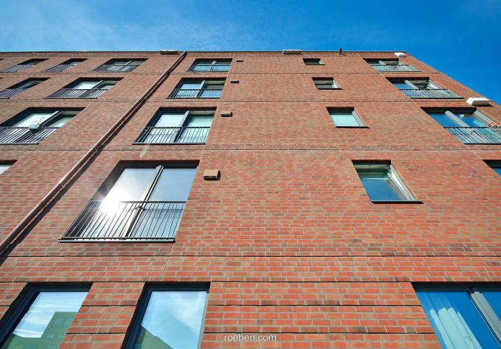 Backsteinwohngebäude bei blauem Himmel, Sonnenlicht spiegelt sich in Fenstern.