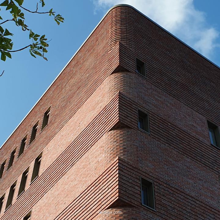 Backsteingebäude mit abgerundeter Ecke, blauer Himmel im Hintergrund.