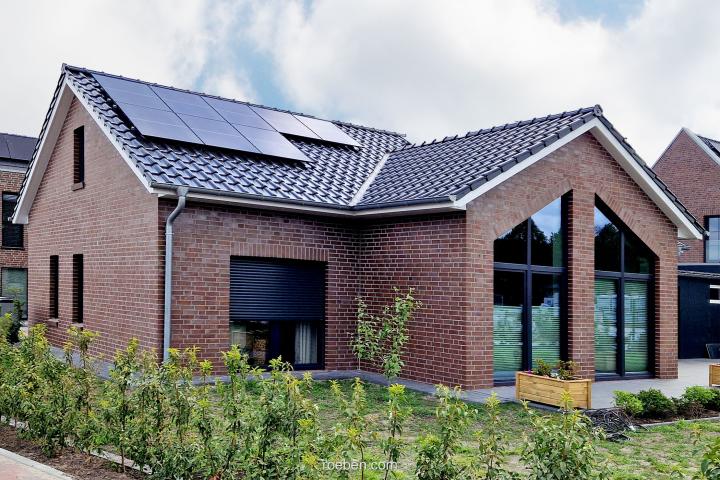 Modernes Backsteinhaus mit Solarpaneelen und großer Fensterfront.