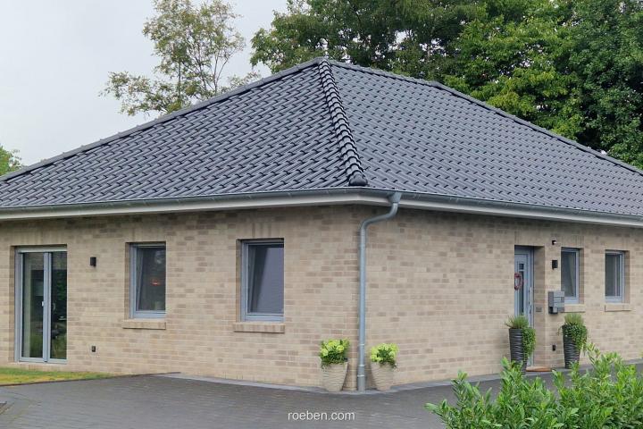 Einfamilienhaus mit grauem Dach und Backsteinfassade, umgeben von Bäumen.