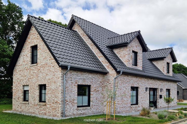 Modernes Backsteinhaus mit grauem Dach, umgeben von Rasen und Bäumen.