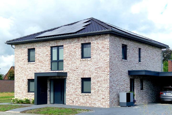 Zweistöckiges helles Ziegelhaus mit Solarpanelen und Carport.