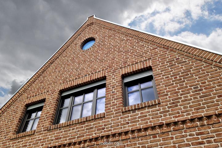 Backsteinhaus mit schwarzem Dach und bewölktem Himmel.