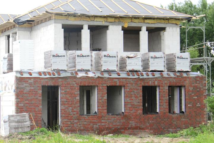 Einfach und wirkungsvoll: Das Abdecken des Mauerwerkes in der Bauphase verhindert, dass Regenwasser eindringt und es später zu Ausblühungen kommt. Unfertiges zweistöckiges Haus, untere Etage aus roten Ziegeln, obere aus weißem Stein.