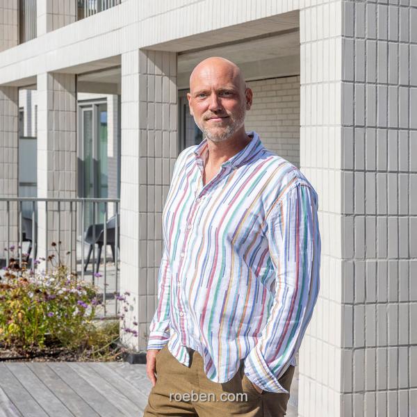 Architekt Marc Koehler in gestreiftem Hemd steht vor modernem Gebäude, bei Tageslicht.