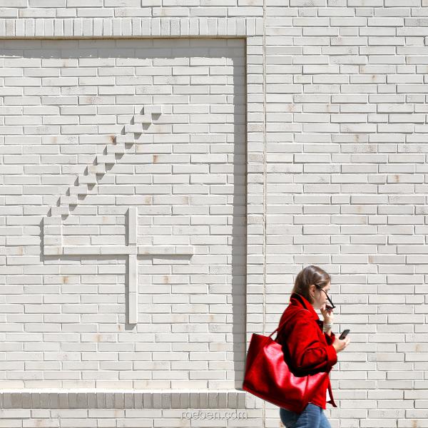 Person mit roter Tasche vor weißer Ziegelmauer mit Relief 4