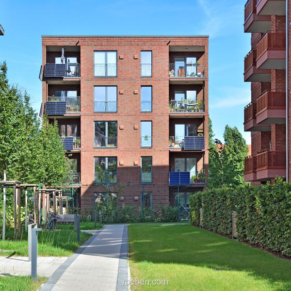 Moderne Wohngebäude aus Backstein mit Balkonen, umgeben von Grünflächen.