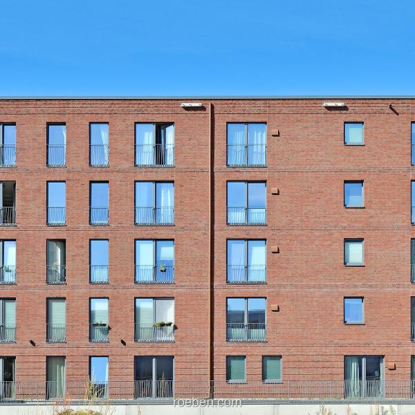 Backstein-Wohngebäude mit vielen Fenstern, blauer Himmel.