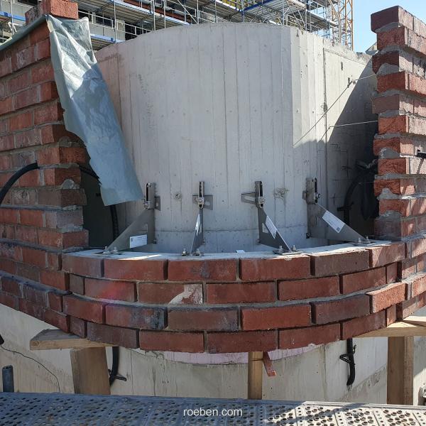 Runde Backsteinmauer im Bau, mit grauer Abdeckung und Metallstangen.