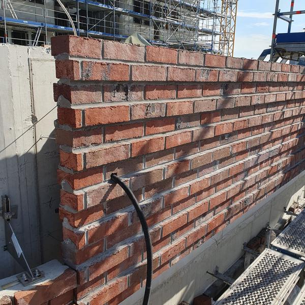 Ziegelmauer im Bau vor einem Gerüst bei Sonnenschein.