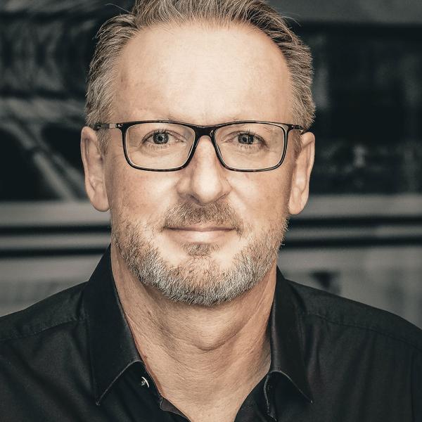 Uwe Stoll mit Brille und Bart, trägt ein dunkles Hemd.