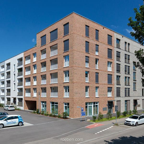 Moderne Wohngebäude unter klarem, blauem Himmel, Autos parken davor.